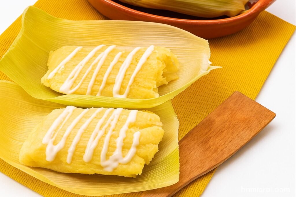Two traditional Honduran montucas drizzled with cream, served on corn husks on a wooden board.