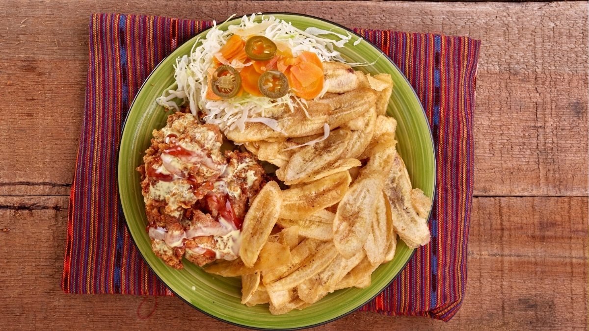 Plato de Pollo Chuco servido con tajadas de guineo, ensalada de repollo y aderezos al estilo hondureño.